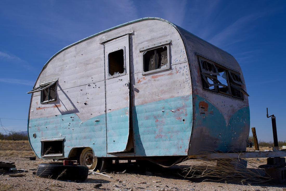 Old, weathered trailer with broken windows under blue sky